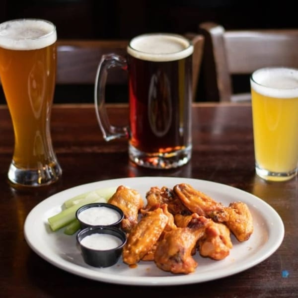 A plate of Half Moon Restaurant & Brewery's chicken wings with celery and dipping sauces, alongside three beers.