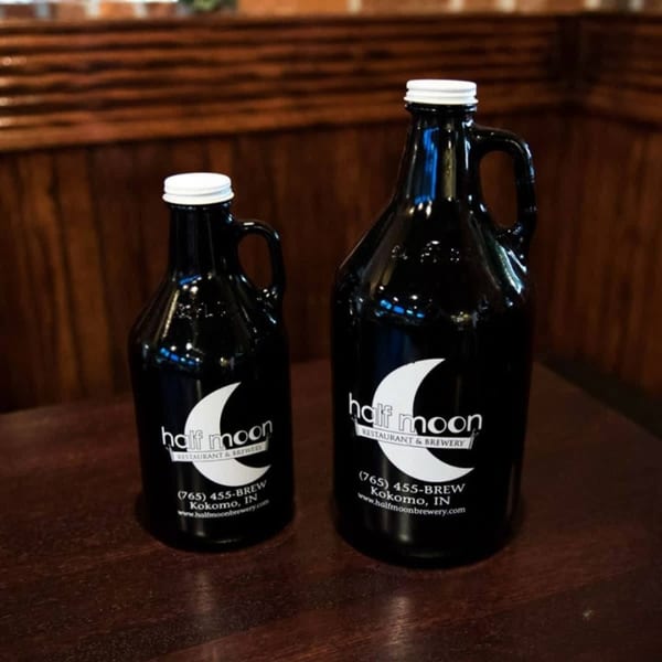 Two black Half Moon Restaurant & Brewery growlers with white caps sit on a wooden table.