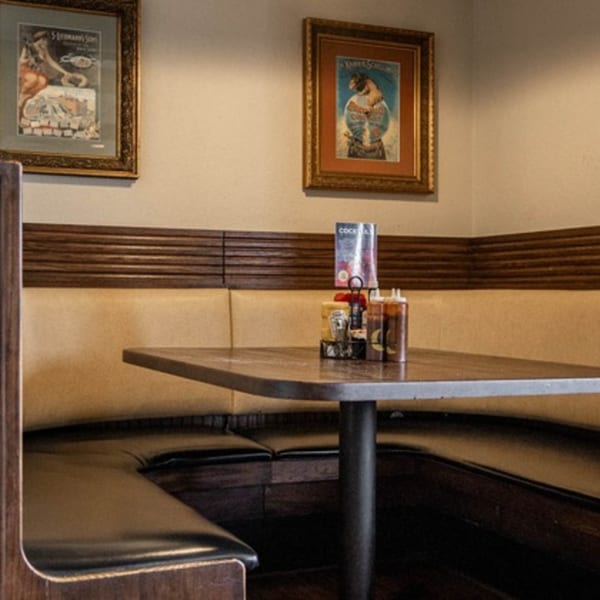 A cozy corner booth with tan and dark brown upholstery, a table, and framed art on the wall.